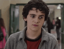 a young man with curly hair is standing in a hallway