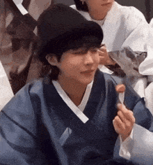 a man wearing a hat and a blue kimono is eating a piece of food with a spoon .