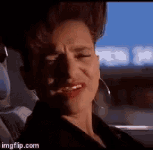 a woman is sitting in a car with her eyes closed and making a funny face .