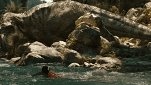 a woman is swimming in a river with a large dinosaur in the background