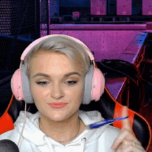 a woman wearing pink headphones holds a pen in her hand