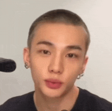 a close up of a young man with a shaved head and earrings .