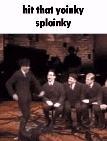 a group of men are sitting in chairs and dancing on a stage with the words `` hit that yoinky sploinky '' above them .