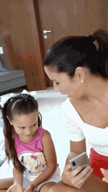 a woman and a little girl are looking at a cell phone .