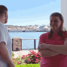 a woman in a pink shirt is standing in front of a lake