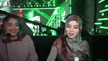two women wearing headphones and a hijab are sitting in front of a green background