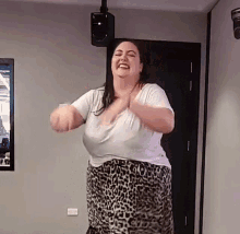 a woman in a leopard print skirt and white shirt is dancing in a room .