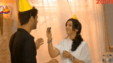 a man and a woman wearing party hats are standing next to each other in front of a sign that says zoon
