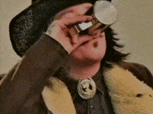 a man wearing a cowboy hat and a fur coat is drinking from a bottle