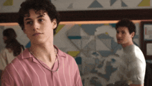 a young man in a pink striped shirt stands in front of a wall with geometric shapes