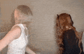 two women are standing next to each other in a room and one of them is wearing a wig .