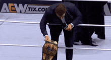 a man in a suit is standing in a wrestling ring with a aew tix.com advertisement behind him