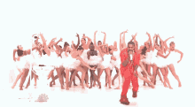 a man in a red suit is singing into a microphone in front of a group of white ballerinas