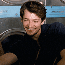 a man smiles in front of a laundromat machine that says speed dry