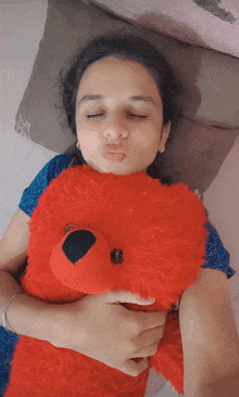 a woman laying on a bed holding a red teddy bear with her eyes closed