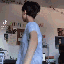 a man in a blue shirt is standing in a room with a laptop and a computer .