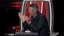 a man applauds while sitting in a chair that says the voice