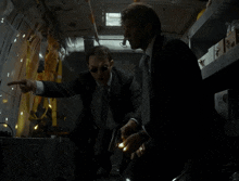 a man in a suit is holding a gun in front of a wall with bullet holes