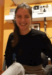 a girl in a black shirt is smiling in front of a shelf