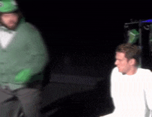 a man wearing a green frog hat is standing next to another man in a white shirt