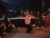 a man in a white shirt is squatting down with his arms in the air in front of a crowd of people