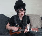 a man wearing a top hat and glasses plays a guitar