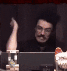 a man is sitting in front of a laptop with his hand up in the air