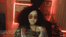 a girl wearing sunglasses is standing in front of a wall that says happy halloween