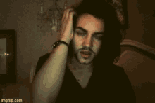 a man with long black hair and a beard is holding his head .
