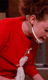 a woman in a red shirt is holding a mop and talking on a cell phone .
