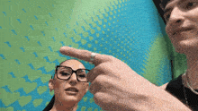 a woman wearing glasses and a ring is pointing at a man