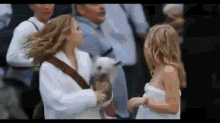 two young girls are standing next to each other in a crowd . one of the girls is holding a small dog .