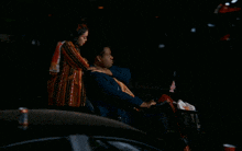 a woman standing next to a man in a wheelchair with a chevrolet car in the background