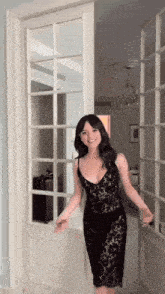 a woman in a black lace dress is standing in front of a glass door