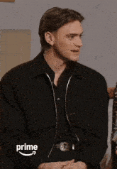 a man wearing a black shirt and a black jacket with the word prime on the bottom