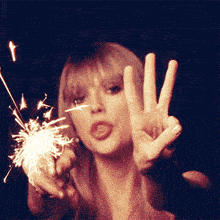 a woman is holding a sparkler in her hand and making a peace sign