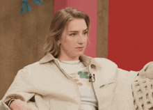a woman wearing a white jacket and a white t-shirt with a green leaf on it is sitting in a chair