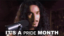 a man with long hair and a mustache is singing into a microphone and the words it 's a pride month are below him