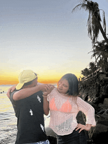 a man wearing a yellow hat is hugging a woman in a pink top