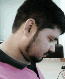 a man with a beard wearing a pink shirt looks down