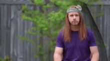 a man with long red hair and a flower in his hair is standing in front of a fence .