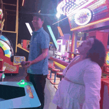 a man and a woman are playing a game in an amusement park with a sign that says pinball