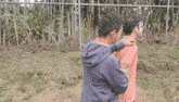 two men are standing next to each other in front of a fence .
