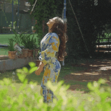 a woman in a blue and yellow floral dress stands in a garden