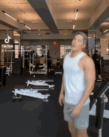 a man in a white tank top is standing in a gym with a tiktok logo on the wall
