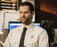 a man in a striped shirt and tie is standing in front of a computer monitor
