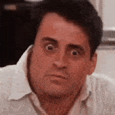 a man in a white shirt is making a funny face while looking at the camera .