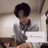 a man is holding a sign that says `` add a comment '' while sitting at a table .