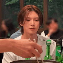 a man is sitting at a table eating food with chopsticks and a bottle of beer .