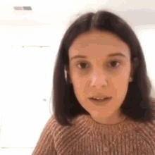 a close up of a person wearing a brown sweater and looking at the camera .